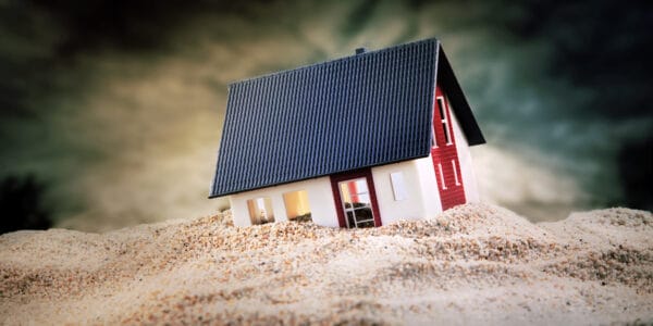 Miniature of house standing in pile of sand